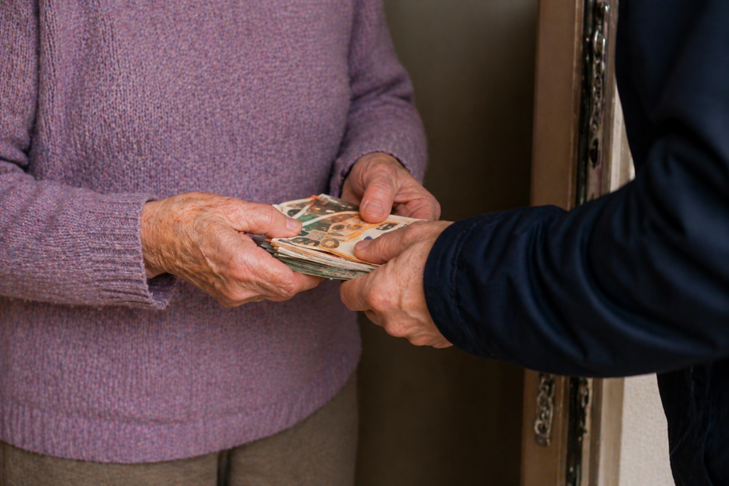 Ältere Person übergibt Bargeld an Betrüger an der Haustür